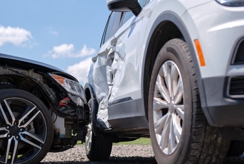Two cars in a collision. One car is severely dented along the side. 