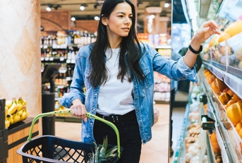 young woman holding grocery basket in a store while picking grocery