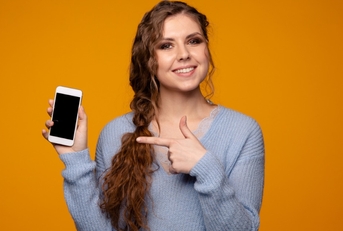smiling young woman wearing grey sweatshirt holding smartphone