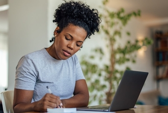 african american woman writing on notepad in front of laptop