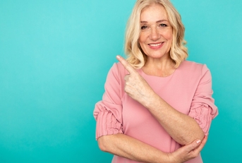 happy woman in short hair raising finger at pink backdrop