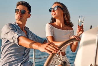 happy couple wearing shades while holding glass of champagne partying on yacht