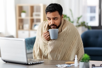 man in blanket with laptop drinking hot tea