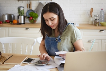 young beautiful woman working on calculator sitting on chair with laptop and papers on table