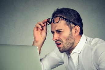 man with glasses squinting eyes at laptop 