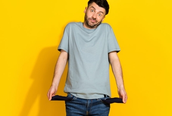 young man standing in front of yellow background showing empty pockets