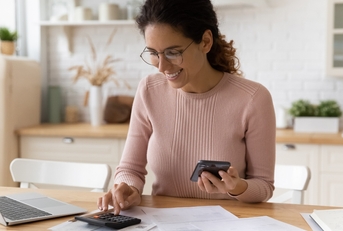 female works with financial papers at home counting on calculator