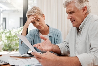 senior couple sitting at table with papers stressing at documents in hands