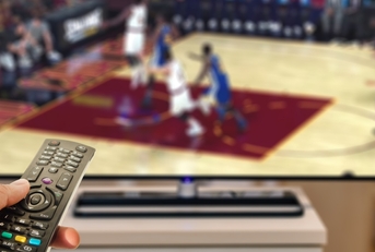 Hand holding a remote in front of a TV playing basketball