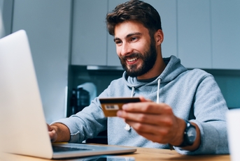 young man paying bills online with credit card and laptop