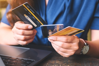 woman holding and choosing credit cards while using laptop