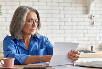 senior lady sitting at table with laptop calculator and cup reviewing taxes at home