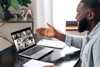 happy african american man sitting on work desk at office using laptop to have virtual video conference with colleagues