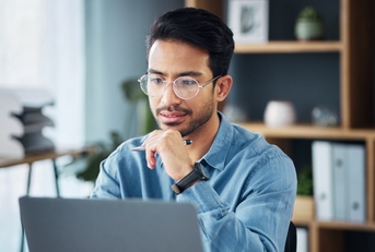 young asian businessman sitting at work desk using laptop for work besides coffee cup
