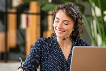 female customer service representative at office using laptop writing on notepad