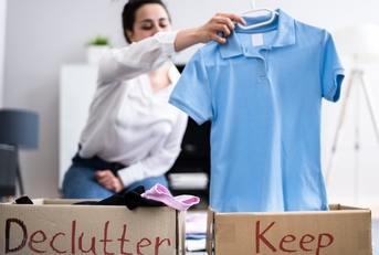 Woman sorting wardrobe into brown boxes with "declutter" and "keep" labels.