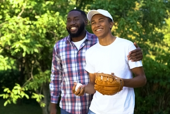 happy father praising son playing baseball in park