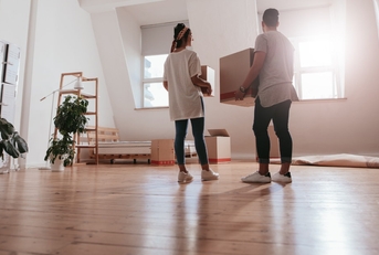 young couple standing in spacious lounge of new house holding moving boxes