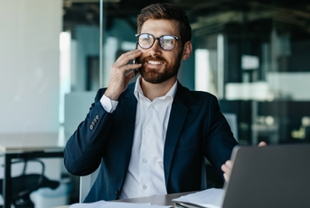 young handsome businessman talking on phone sitting at table with laptop and papers in office