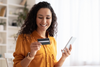 Smiling woman looking at credit card and holding phone