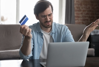 man annoyed at laptop while holding card in hand 
