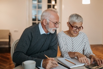 senior couple sitting at table calculating bills using calculator 
