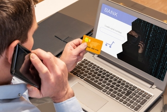 man using laptop holding card while talking on smartphone and getting scammed