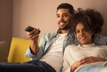african american couple sitting on couch at home using remote while watching tv