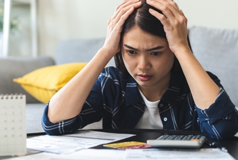 young woman stressed by calculating expenses on table