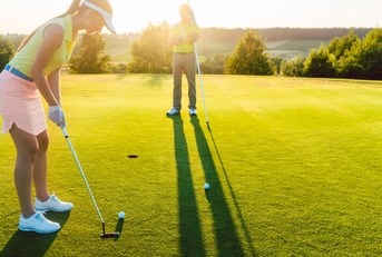 female golf player playing golf at golf course with male instructor in background