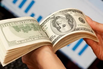 man skimming through cash notes in hand with laptop in background