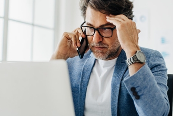business man holding head in stress while using laptop and talking on smartphone at office