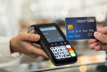 A credit card is held up to a handheld credit card reader. This appears to be at a store checkout.