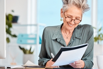 happy senior business woman sitting in office making notes while holding file