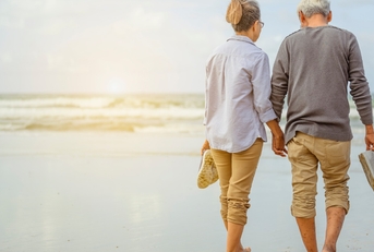 senior couple walking on beach while holding each others hand