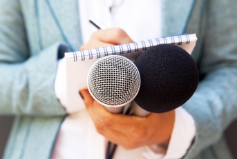 female journalist holding mics while making notes for interview