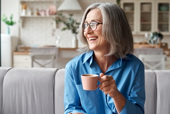 grey-haired woman drinking coffee relaxing on sofa