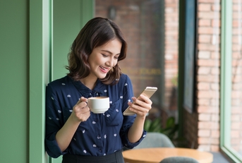 Woman smiling and holding a cup of coffee while looking at phone