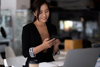 Business asian woman using mobile phone with a laptop on the table,while working in her office