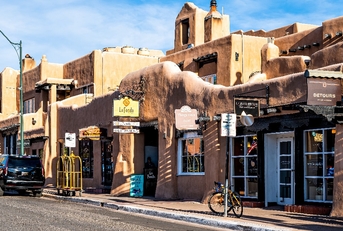 old town streets with adobe style architecture and sign boards besides cars on sidewalks in united states new mexico city during day time