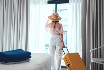 beautiful woman wearing sun hat checking into hotel room with luggage