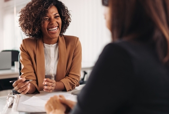 a female financial advisor with short curly hair is consulting a client with joy in her office setting.