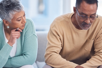 An elderly couple is sitting in the lounge of their house with documents, planning their tax and home budget with the help of a laptop and calculator.