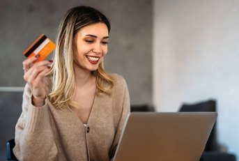 A happy smiling woman holding up a credit card in front of her laptop.