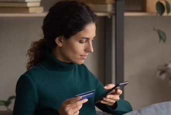 Focused young woman holding a smartphone in one hand and a card with another hand.