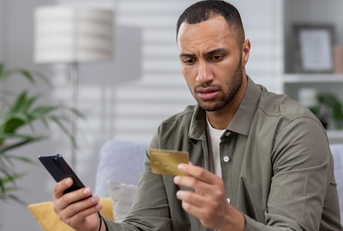 worried man holding card with smartphone