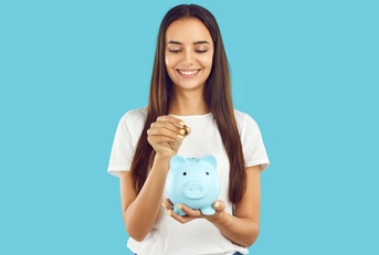 A happy woman is holding a piggy bank and about to insert a coin.