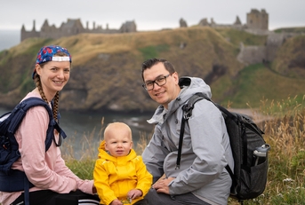 The author with his wife and young son, shown sitting on a bluff overlooking a Scottish castle. They are looking at the camera and smiling.