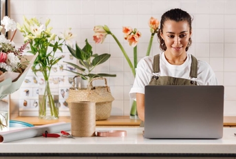 Young flower shop owner using laptop on counter while standing.
