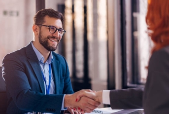A businessman is shaking hands with a woman across a desk.
